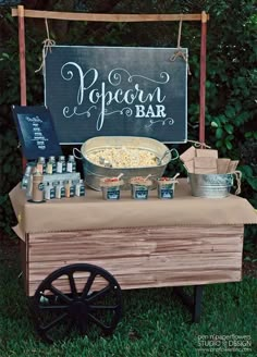 an outdoor popcorn bar is set up on the grass with chalkboard sign above it