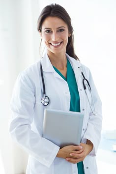 a woman in a white lab coat holding a laptop computer and smiling at the camera