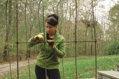 a woman in green jacket holding on to a metal fence with trees and grass behind her