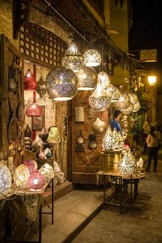 an outdoor market with lots of hanging lights and lamps on display in front of it