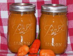 two mason jars filled with hot peppers sitting on a checkered table cloth