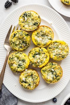 several muffins with cheese and spinach on a white plate next to a fork