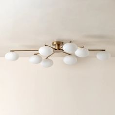 a ceiling light with five white balls hanging from it's center point and four brass arms