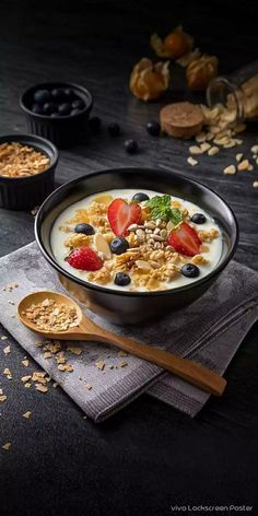 a bowl of oatmeal with strawberries and blueberries in it next to two spoons