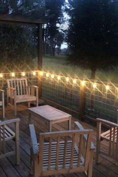 some chairs and tables on a wooden deck with lights strung over the top of them