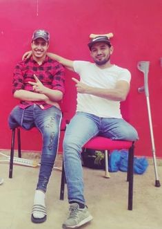 two men sitting on chairs in front of a red wall