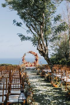 an outdoor ceremony set up with chairs and flowers on the aisle, surrounded by trees