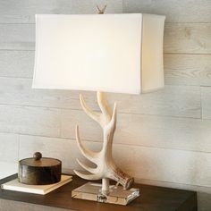 a table lamp with a white shade on it and a deer antlers head next to it