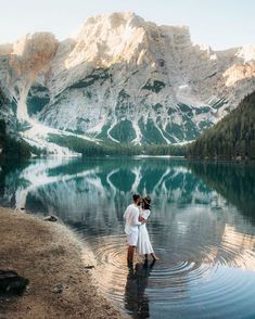 two people standing in the water with mountains in the background