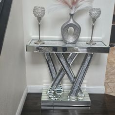 a mirrored table with three silver candlesticks and a vase on top that has a pink feather in it