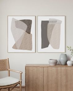 two abstract paintings hang on the wall next to a chair and sideboard with vases