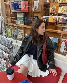 a woman sitting on top of a red bench in front of a book store window