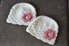 two white crocheted hats with pink flowers on the top and bottom, sitting on a couch