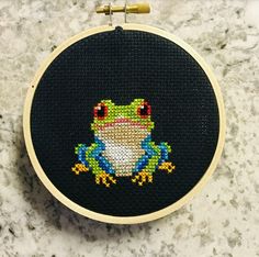 a cross stitch frog sitting on top of a counter