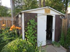 an outhouse with vines growing on the wall and doors open in a garden area