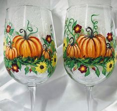 two wine glasses painted with pumpkins and flowers on white fabric background, one is empty