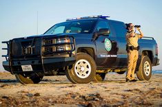 a police officer standing next to a truck on the beach with his camera in hand