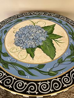 a blue and black plate with flowers painted on the side, sitting on a carpeted floor