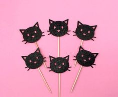 four black cat cupcake toppers on a pink background