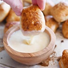 a person dipping something into a bowl with some bread on the side and other pastries in the background