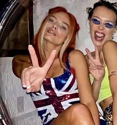 two beautiful young women sitting next to each other in front of a mirror giving the peace sign