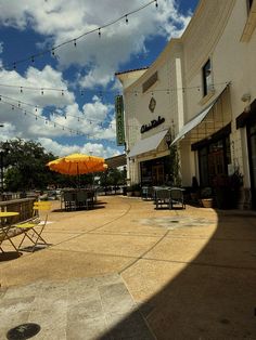 an outdoor patio with tables and umbrellas in front of a building on a cloudy day