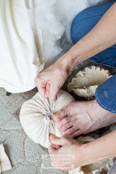 a woman is making something with her hands while sitting on the floor next to other items