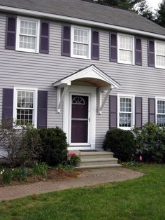 a gray house with white trim and purple shutters on the front door is shown