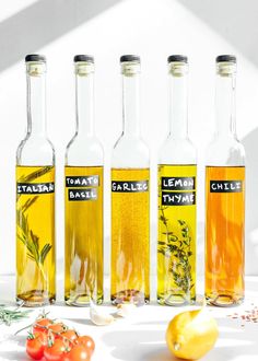 four bottles filled with different types of olive oil next to tomatoes and lemons on a table