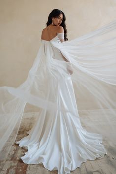 a woman in a white wedding dress is holding her veil over her shoulder and looking off to the side