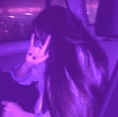 a woman sitting in a car holding her hand up to her face and making the peace sign