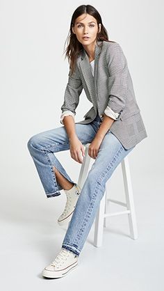 a woman sitting on top of a white stool wearing jeans and a blazer jacket