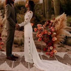 a man and woman standing next to each other in front of a desert setting with flowers