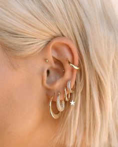 a woman with blonde hair wearing gold ear cuffs and an earring that has three stars on it