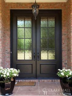 two large black vases with white flowers in front of a double door and brick wall