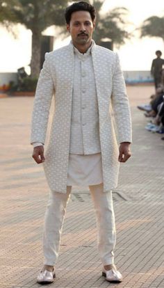 a man in a white suit standing on a brick walkway with his hands behind his back