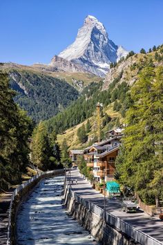 a river running through a lush green forest covered hillside next to a tall snow capped mountain