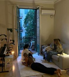 two women sitting on the floor in front of a living room with a piano and windows