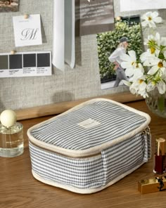 a white and black checkered bag sitting on top of a wooden desk next to a vase with flowers