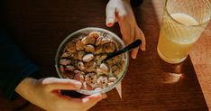 two hands holding a bowl of food next to a glass of orange juice on a table