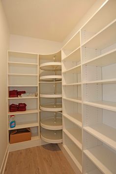 an empty walk in closet with white shelving and wood flooring on the side