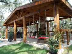 a large wooden structure with swings in the grass and trees around it, next to a swimming pool