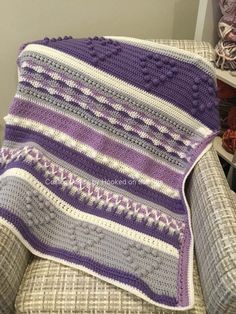 a crocheted blanket sitting on top of a couch next to a pile of yarn