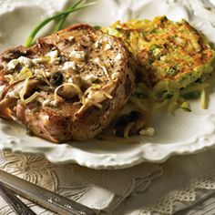 two steaks on a white plate with potatoes and green beans in the background, next to a fork