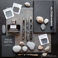 some rocks, pens and ink are on a table with other items that have been placed around them