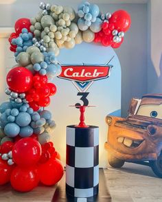 the balloon arch is decorated with cars balloons and an auto race car sign that reads caler