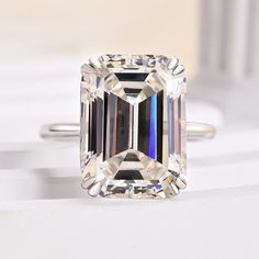 an emerald - cut diamond ring sits on a white surface