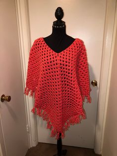 a red crocheted ponchy on a mannequin stand in front of a door