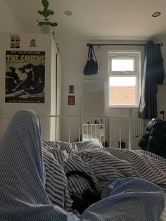 an unmade bed with blue and white sheets in a bedroom next to a window