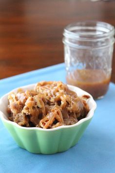 a green bowl filled with food sitting on top of a blue place mat next to a jar of peanut butter